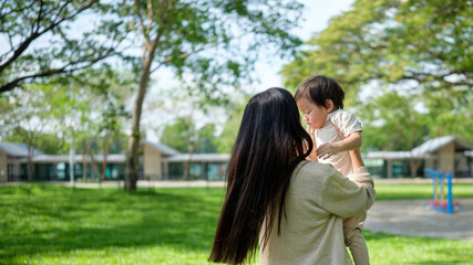 Naklejka premium Tender moment of a mom holding her toddler while surrounded by greenery and trees.