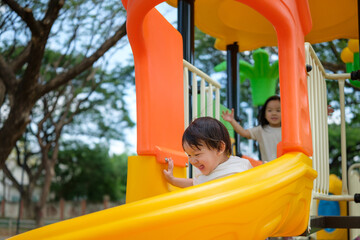 Excited little boy sliding down a bright yellow playground slide with joy.