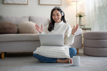 Happy woman wearing headphones enjoying a video call while sitting comfortably at home.