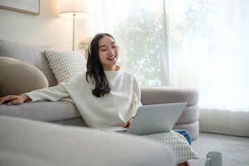 Happy young woman enjoying screen time while relaxing at home with a laptop.