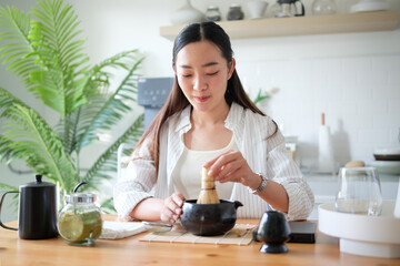 Young woman whisking matcha tea using a traditional bamboo chasen in a bright modern kitchen.