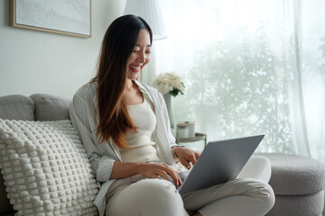 Obraz premium Relaxed woman using a laptop at home in a cozy, sunlit space with minimal decor.