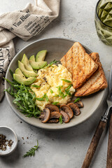 Scrambled eggs, toasts, avocado and mushrooms on rustic plate for homemade breakfast