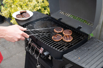 Male grilling burgers on outdoor bbq grill with juicy patties