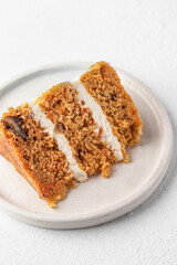 Homemade layered carrot cake with cream cheese, walnuts and spices on a plate on white background