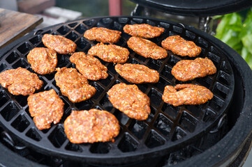 Spicy homemade sausage patties grilling on open flame bbq grill outdoors