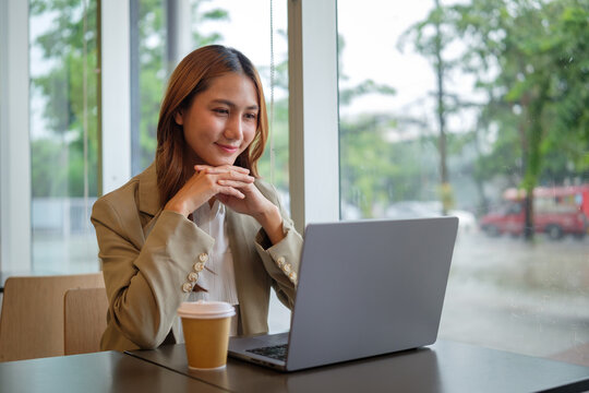 Smiling young businesswoman working with laptop in modern coffee shop.