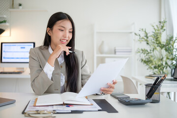 Asian woman in business attire analyzing paperwork and taking notes in a contemporary workspace....