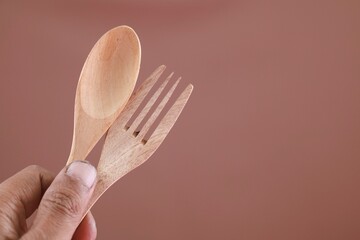 Close up hand holding wooden fork and spoon, eco friendly cutlery on white background. Conscious...