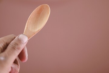Close up hand holding wooden spoon, eco friendly cutlery isolated on brown background. Conscious consumption