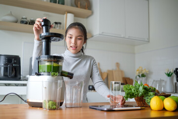 Smiling young woman preparing cold-pressed vegetable juice in a bright modern kitchen. Healthy...