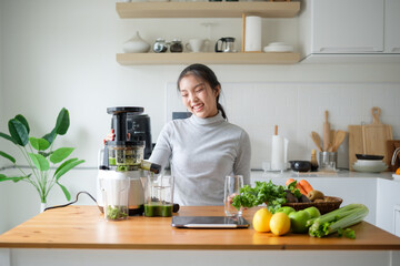 Smiling young woman making healthy cold-pressed juice in a modern kitchen. Healthy lifestyle and...