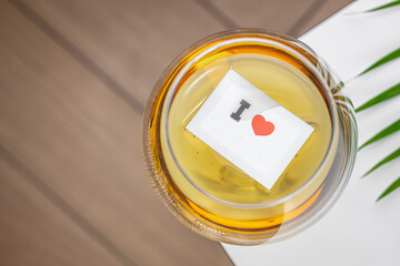 A close-up top view of a glass of white wine with a small paper note featuring love symbol floating...