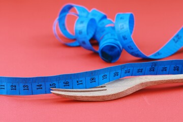 Wooden fork tied with twisted blue measuring tape isolate on red background. Diet and fit body...
