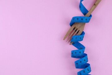 Wooden fork tied with twisted blue measuring tape isolate on pink background. Diet and fit body...
