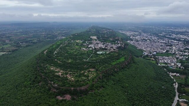 Vast Walled fortress with small town on lush green mountain top, rajasthan, India. Drone aerial. Reveal.