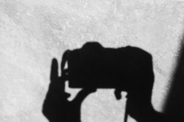 Shadow of a photographer holding a camera against a textured wall, in black and white. A black and white image featuring the silhouette of a person holding a camera, with the background being a wall.