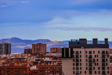 Various houses of a Spanish town against the backdrop of mountains under a cloudy sky	
