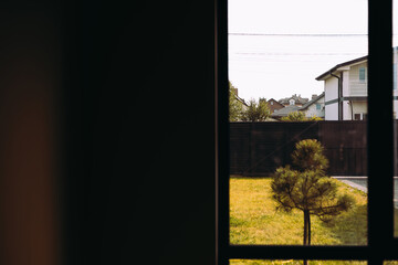 A serene suburban scene is viewed through a window, featuring houses, yards, green grass. A view...