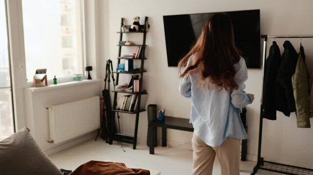 A woman takes off her jacket and throws it on the sofa, then chooses clothes on hangers and clicks on her phone