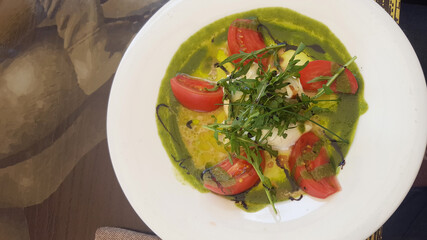 A plate of vibrant green sauce topped with sliced tomatoes and fresh herbs. The dish is presented on a white plate, showcasing a colorful culinary creation.