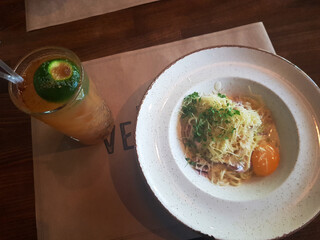 A bowl of noodles topped with vegetables and an egg, accompanied by a refreshing drink with a lime...