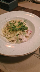 A plate of creamy pasta topped with herbs and vegetables. The dish is served in a white bowl on a wooden table.