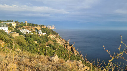 Coastal landscape with cliffs, green vegetation, and a calm sea under a cloudy sky. The scene...