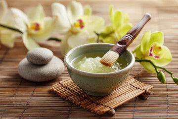 Green spa treatment in a ceramic bowl with a brush, surrounded by smooth stones and delicate orchids