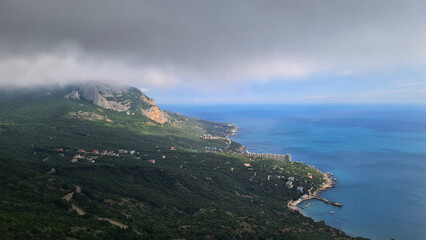 A scenic coastal view featuring a rocky shoreline, lush green hills, and a cloudy sky over the blue...
