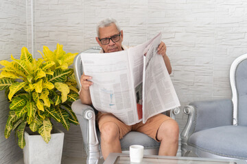 Senior man reading newspaper at home, sitting comfortably in armchair