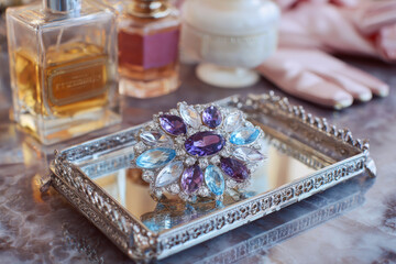 Elegant vintage brooch adorned with colorful gemstones displayed on a decorative silver tray, surrounded by perfume bottles