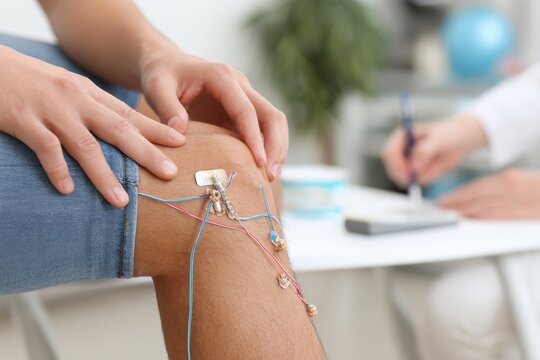 Individual undergoing therapeutic treatment with electrodes attached to the knee, showcasing modern physiotherapy techniques in a clinical setting for recovery and rehabilitation.