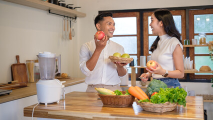 Happy young couple preparing fresh fruits and vegetables together in a modern kitchen. Smiling and talking while making healthy meals.
