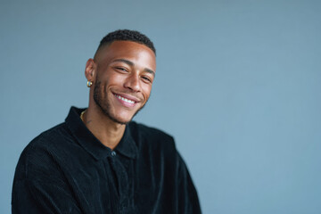 Obraz premium Young man smiling wearing black shirt and gold earring on blue background