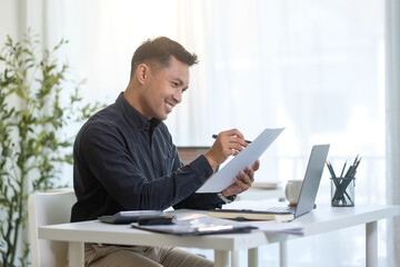 Smiling financial analyst reviewing data and charts while enjoying coffee at his desk.