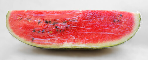 ripe slice of red watermelon wrapped with the catering transparent film. isolated on white wall...