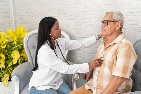Female doctor examining senior patient with stethoscope at home