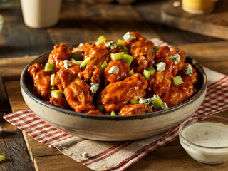 Buffalo chicken wings in a bowl topped with celery and blue cheese crumbles, served on a rustic table with ranch dipping sauce