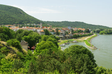 A panoramic view of Hainburg an der Donau, featuring the town nestled between a lush green hill and...