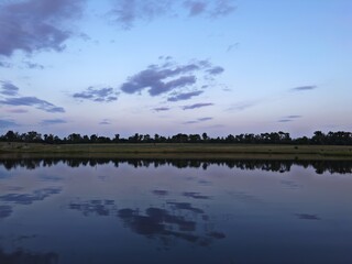A calm pond mirrors the darkening evening sky, highlighting the quiet beauty of nature as daylight...