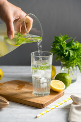 Lemonade with lemons, limes and fresh mint. Pouring homemade lemonade in a glass