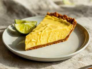 A slice of creamy key lime pie with a graham cracker crust, served on a white plate with fresh lime wedges in warm natural light