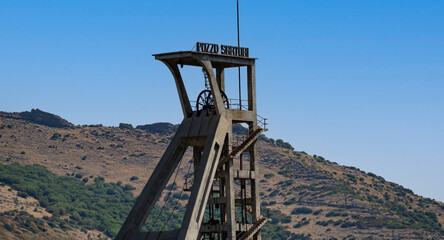 Rusty industrial tower stands isolated against a dry hillside covered with sparse vegetation
