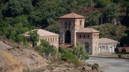 Rusty industrial tower stands isolated against a dry hillside covered with sparse vegetation
