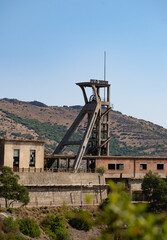 Rusty industrial tower stands isolated against a dry hillside covered with sparse vegetation
