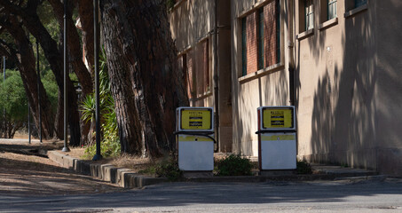 Old gasoline and diesel pumps stand unused near a worn building and pine trees