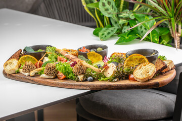 A beautifully arranged gourmet appetizer platter with assorted cheeses, pate, bread, fresh fruits, greens, and dips, served on a rustic wooden board in an elegant setting