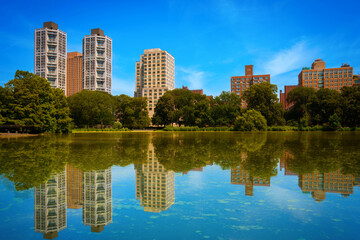 New York City skyline and Central Park landscape with building reflections over Harlem Meer Lake — a tranquil summer scene in Upper Manhattan