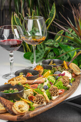 A luxurious appetizer platter with assorted cheeses, pate, bread, fruits, and greens served on a rustic board, accompanied by elegant glasses of red and white wine